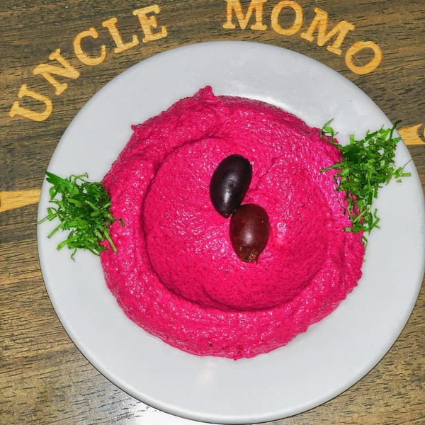 Vibrant pink Lebanese beet hummus, garnished with two olives and fresh parsley, on a white plate.