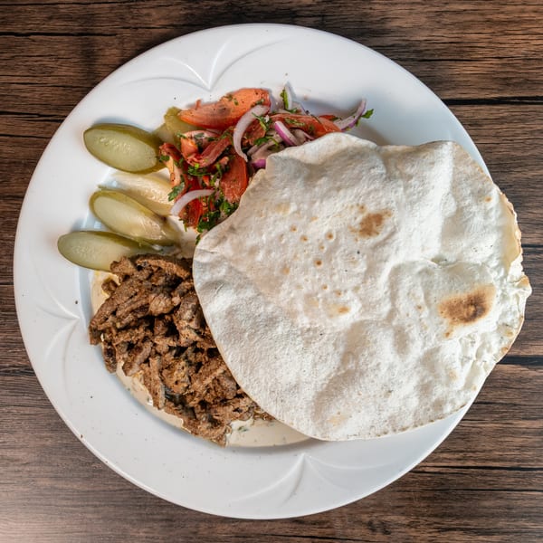 Lebanese shawarma plate with sliced meat, pita bread, pickles, and a tomato and onion salad.