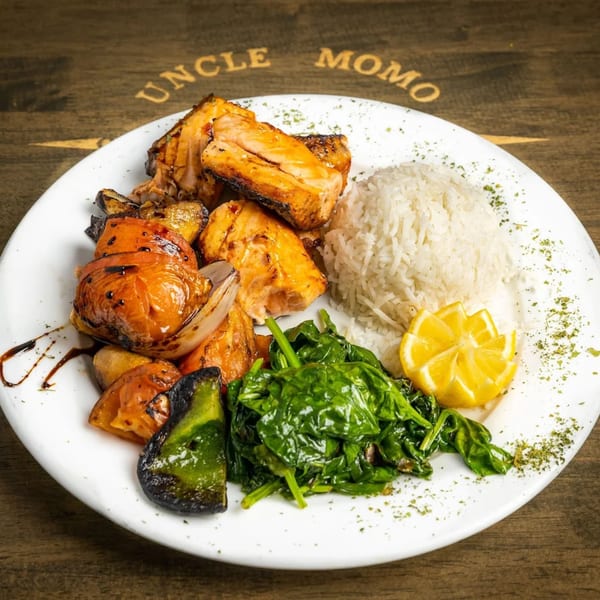 Uncle Momo's Lebanese grilled salmon with rice, spinach, roasted vegetables, and a lemon wedge.