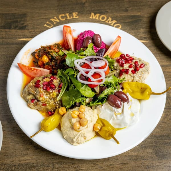 A white plate of Lebanese mezze, including hummus, baba ghanoush, labneh, and salad, on a wooden table.