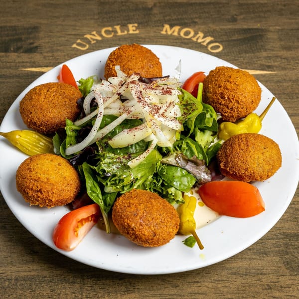 A white plate of Lebanese falafel, salad with onions, tomatoes, and pickled peppers on a wooden table.