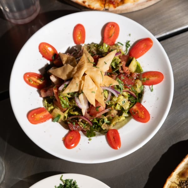 Lebanese Fattoush salad with lettuce, tomatoes, red onions, and crispy pita bread on a white plate.