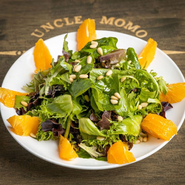 Uncle Momo's Lebanese salad with mixed greens, pine nuts, and orange segments on a white plate.