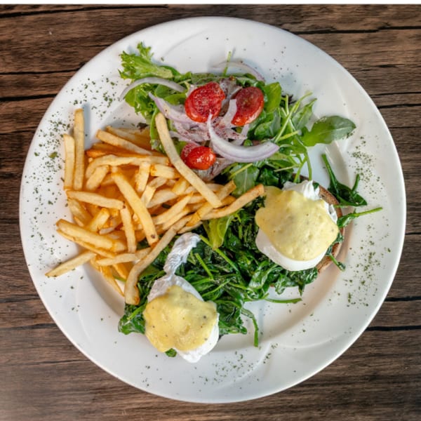 Eggs Benedict with spinach, fries, and a side salad with cherry tomatoes and red onions.