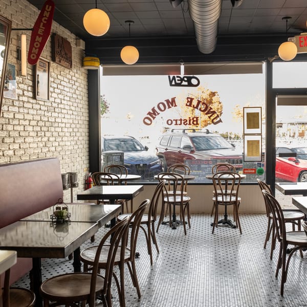 Interior of Uncle Momo restaurant with tables, chairs, and a large window showing street parking outside.