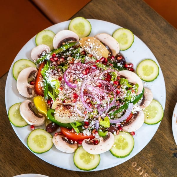 A vibrant Lebanese salad with lettuce, vegetables, pomegranate, and feta cheese, garnished with cucumber slices.