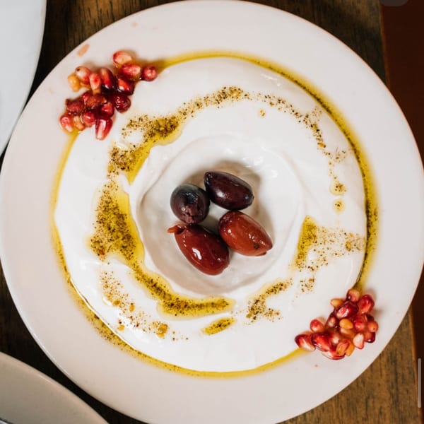 Labneh dip with olives, pomegranate seeds, olive oil, and spices on a white plate.