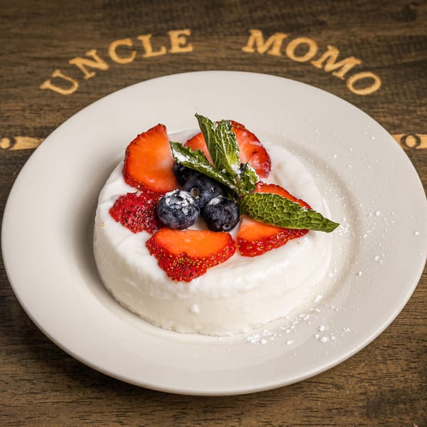 White dessert topped with strawberries, blueberries, mint, and powdered sugar on a white plate.