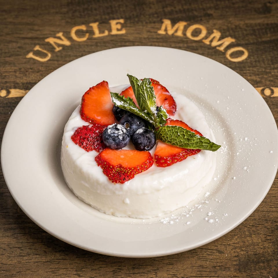 White dessert topped with strawberries, blueberries, mint, and powdered sugar on a white plate.