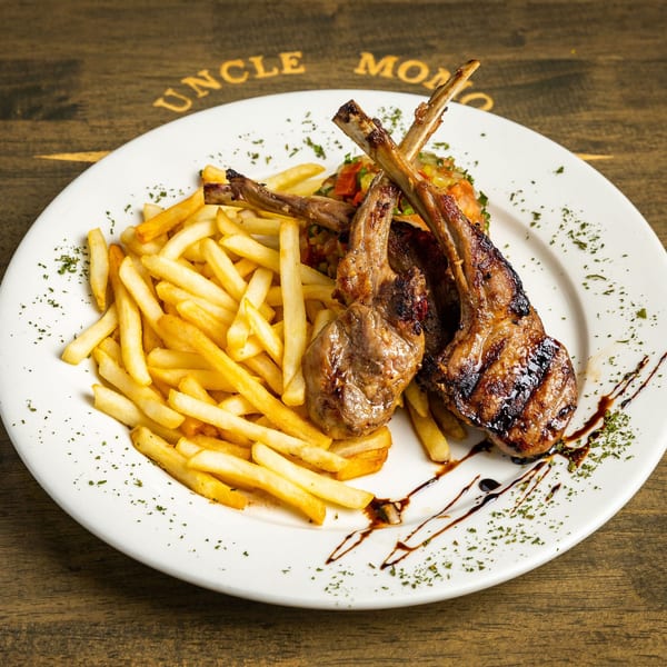 Grilled lamb chops with french fries and a side of colorful diced vegetables on a white plate.