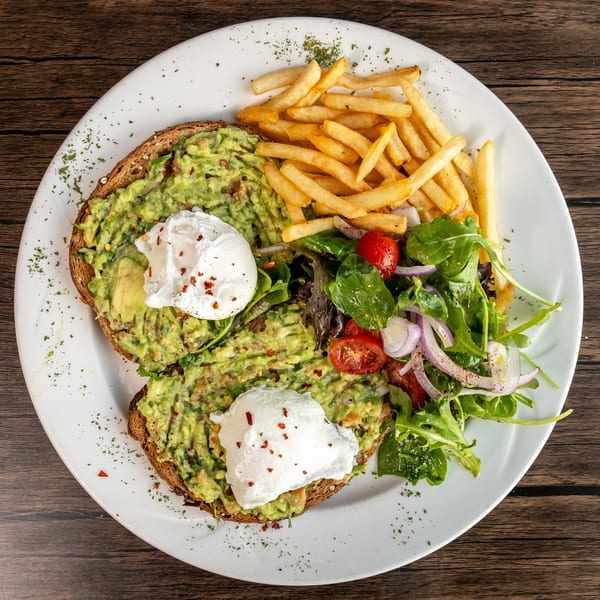 Avocado toast with poached eggs, fries, and a side salad on a white plate.